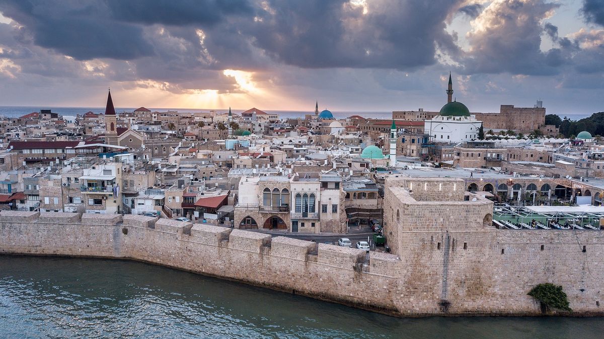 The sea walls of Old Akko at sunset with dramatic clouds, the Al-Jazzar Mosque and churches visible