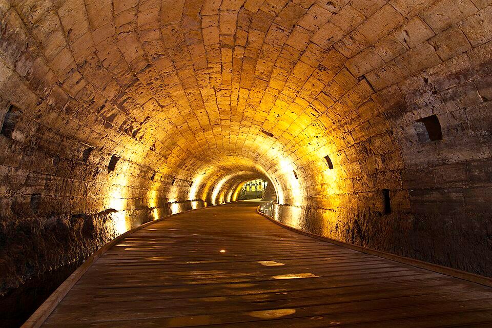 Inside the Templar Tunnel in Akko with illuminated barrel-vaulted ceiling and wooden walkway